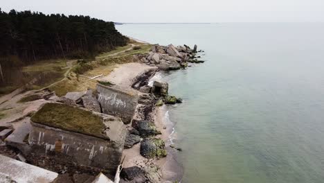 Aerial-view-of-abandoned-seaside-fortification-building-at-Karosta-Northern-Forts-on-the-beach-of-Baltic-sea-in-Liepaja-in-overcast-spring-day,-wide-drone-shot-moving-forward-tilt-down-high