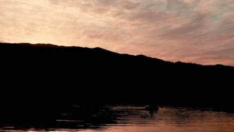 Sunset-silhouetting-the-landscape-and-the-sky-reflecting-off-the-water-while-canoers-casually-paddle-by