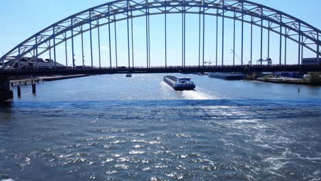 Barge-With-Backwash-Passing-Under-Arch-Bridge-Over-Noord-River-At-Hendrik-Ido-Ambacht,-Netherlands