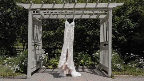 Approaching-a-beautiful-designer-wedding-dress-hanging-from-a-pergola-outdoors-during-a-beautiful-day-at-Strathmere-Wedding-and-Event-center-in-Ottawa,-Canada
