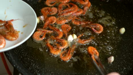 cook-removing-fried-prawns-from-the-heat-and-putting-them-on-a-plate-during-the-preparation-of-fideua