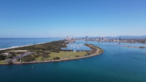 High-static-drone-view-of-a-man-made-ocean-inlet-and-safe-boat-harbor-with-a-metropolitan-skyline-and-mountain-range-in-the-distance