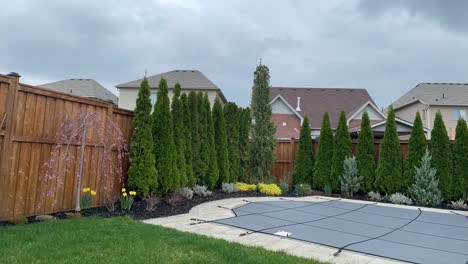 Pool-cover-covering-closed-pool-in-early-to-mid-spring-with-spring-rain---light-april-showers-time-lapse-of-backyard-with-pool-with-emerald-cedars-around-fence-wall-and-garden