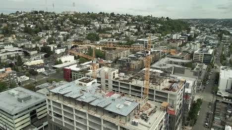 Slowly-pulling-back-and-revealing-two-tower-cranes-erecting-a-high-rise-building-in-Seattle,-aerail