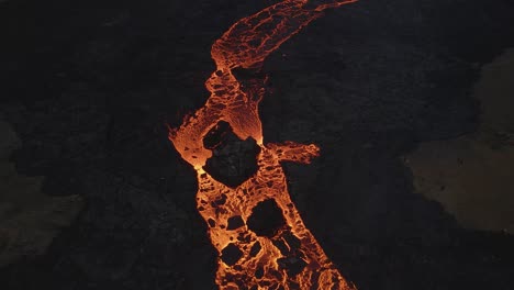 Aerial-top-down-forward-over-lava-river-flowing-along-black-volcanic-landscape