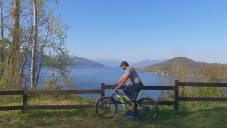 Man-on-bicycle-arrives-and-stops-to-enjoy-amazing-panoramic-view-over-Maggiore-lake,-Italy