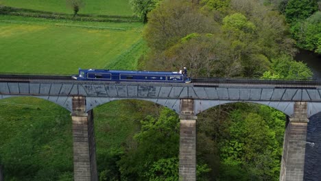 Aerial-view-following-narrow-boat-on-Trevor-basin-Pontcysyllte-aqueduct-crossing-in-Welsh-valley-countryside-slow-tracking-pan-left