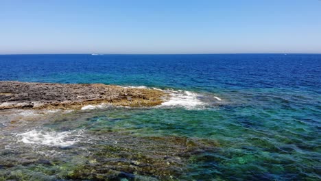 Aerial-forward-view-of-waves-splashing-rocky-limestone-emerald-blue-beach-in-Sliema,-Malta