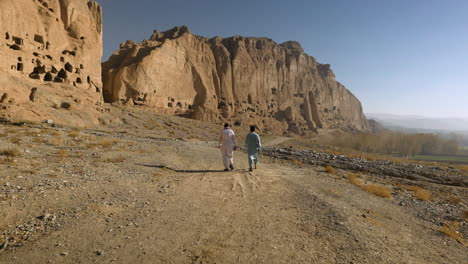 Dos-Hombres-Caminando-En-El-Valle-De-Bamyan-Con-Vistas-Al-Sitio-De-Buda-De-Bamyan-En-Afganistán
