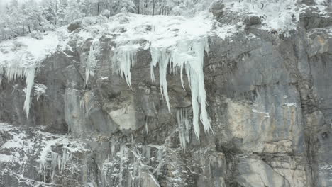 Low-angle-aerial-of-large-icicles-hanging-of-mountain-ridge