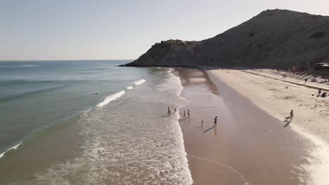 Gente-Jugando-En-La-Playa-De-Burgau,-Algarve,-Besada-Por-La-Suave-Luz-Del-Sol