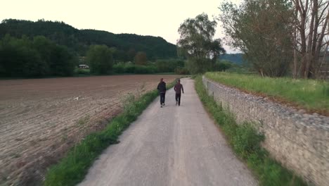 Two-people-running-on-rural-countryside-dirt-track-in-golden-hour-next-to-field
