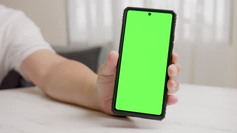 Man's-hand-shows-mobile-smartphone-with-green-screen-in-vertical-position-isolated-on-green-background