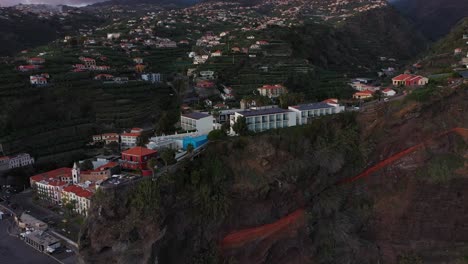 A-circling-drone-shot-of-a-hotel-on-top-of-the-steep-cliff-in-Ponta-do-Sol-in-Madeira-during-the-last-rays-of-sunshine-from-the-sunset