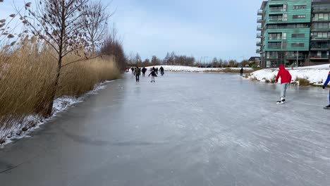 People-skating-and-walking-on-a-frozen-pond-in-a-city-park-during-the-freezing-cold-in-February,-which-lasted-only-one-week-in-the-Netherlands-in-2021