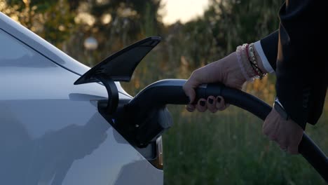 Tesla-electric-vehicle-being-charged-with-countryside-background,-close-up