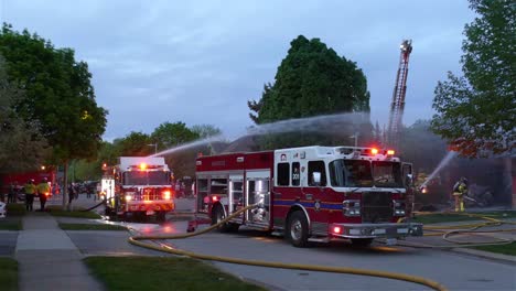 Feuerwehrleute-Und-Feuerwehrleute,-Die-Wasser-Auf-Einen-Hausbrand-Aus-Einem-Feuerwehrauto-Sprühen