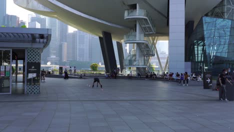 Young-chinese-man-roller-skates-collecting-freestyle-cones-from-floor,-Marina-Bay,-Singapore