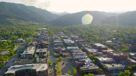 Aerial-shot-of-beautiful-mountain-vista,-bright-green-trees,-and-Pearl-Street-in-downtown-Boulder-Colorado-during-an-evening-sunset-with-warm-light-on-the-rocky-mountain-town-and-summer-landscape