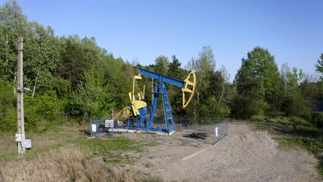 Oil-Pump-Equipment-At-Work-On-The-Landscape-Surrounded-With-Green-Forest-Near-Campina,-Romania