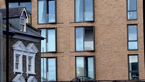 View-Of-A-Man-Through-Glass-Window-Of-An-Apartment-Building-Near-East-Putney-Station-In-London,-UK-With-Trains-Passing-By-In-Foreground
