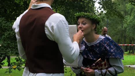 Adult-caucasian-female-dancers-in-traditional-folk-costumes-fixing-makeup-before-a-dance-performance-in-open-air,-sunny-summer-evening,-happy,-Latvian-national-culture,-medium-shot