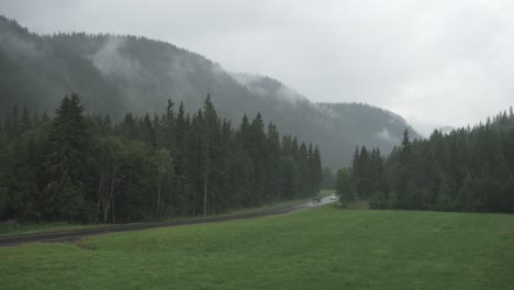Car-passing-through-forest-road-beside-a-mountain-range-in-a-rainy-day,-wide-shot