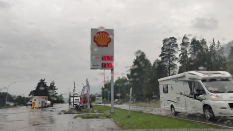 Frustration-over-high-fuel-prices---Shell-billboard-seen-from-inside-car-with-rain-on-front-window-and-passing-traffic---Static-rainy-day-clip-with-passing-traffic-Norway