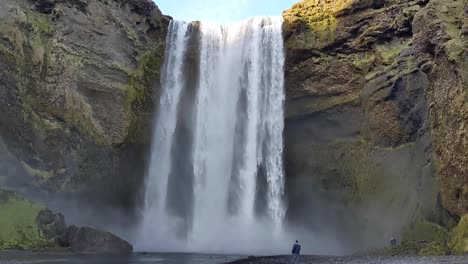 Skogafoss-Waterfall-in-Iceland-in-Summer-with-man-walking-along-river