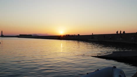 Schöner-Sonnenuntergang-über-Dem-ägäischen-Meer-In-Chania,-Touristen,-Die-Den-Alten-Venezianischen-Hafen-Mit-Historischem-Leuchtturm-Während-Des-Sommerabends-Genießen,-Besichtigungspunkt-In-Griechenland