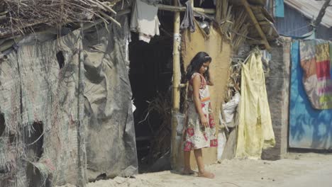 Armes-Asiatisches-Mädchen-Mit-Dunkler-Haut-Kommt-Barfuß-Aus-Ihrer-Hütte-Und-Schaut-Nach-Draußen,-Slumgebiet