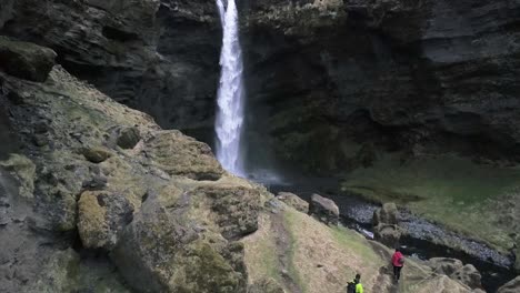 Two-People-hiking-up-green-moss-covered-canyon-in-Iceland-to-Kvernufoss-Waterfall