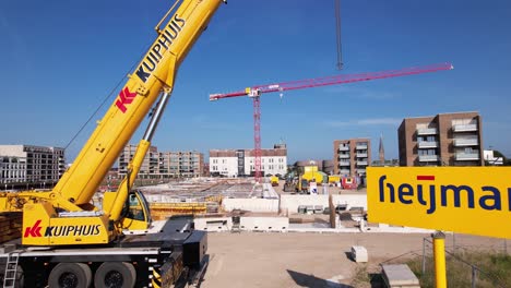 Slow-aerial-approach-and-passing-between-sign-with-company-name-and-heavy-machinery-revealing-construction-site-of-luxury-apartment-Kade-Zuid-complex-being-build-with-large-red-crane-in-the-background