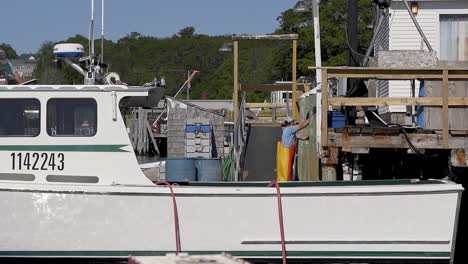 Kommerzielle-Hummerfischer-Entladen-Ihren-Fang-Für-Den-Tag-In-Einem-Kleinen-Hafen-An-Der-Küste-Von-Maine,-Wie-Von-Einem-Anderen-Boot-Auf-Dem-Wasser-Aus-Gesehen