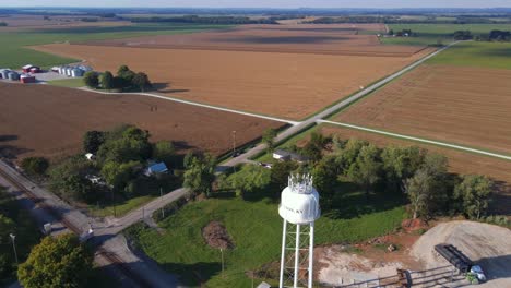 Aerial-4K-fast-rotating-drone-footage-of-a-farm-where-a-water-tower-and-many-silos-can-be-seen-in-a-rural-environment
