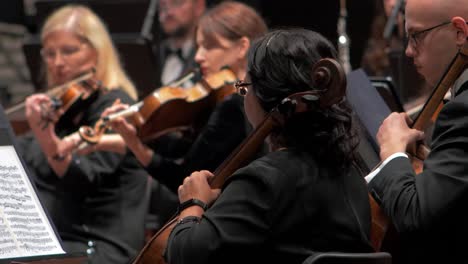 Focus-a-female-musicians-playing-the-violin-with-an-orchestra,-Liepāja-Symphony-Orchestra-season-opening-concert,-concert-hall-Great-Amber-,-medium-shot,-rack-focus-on-cello-player