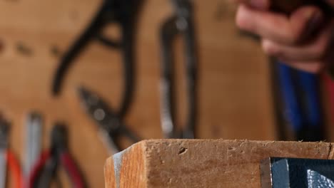 Caucasian-hand-hammering-a-nail-into-a-piece-of-wood-in-diy-home-workshop