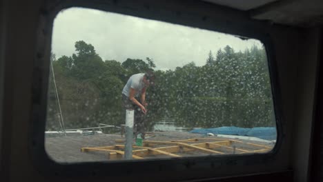View-through-rainy-boat-window-young-man-working