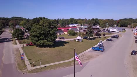 US-flag,-streets-and-houses-in-Grand-Marais,-Michigan,-forward-aerial