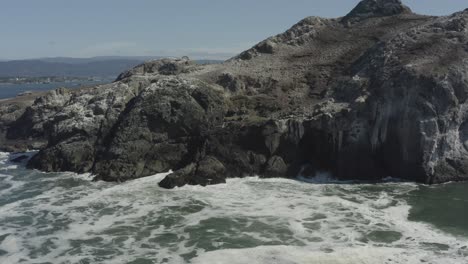 Slowly-approaching-aerial-drone-footage-of-crashing-ocean-waves-on-a-large-boulder-sitting-in-the-Pacific-ocean,-Oregon