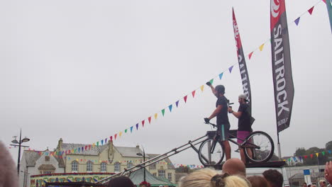 Man-Filming-Skilled-Biker-Performing-Stunt-On-A-Bicycle-During-Mountain-Bike-Stunt-Show-In-Truro,-Cornwall,-England