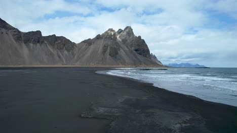 Island-Drohne-über-Schwarzem-Sandstrand-Mit-Wellen,-Die-An-Der-Küste-Zusammenbrechen