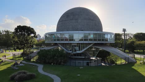 Establishing-low-level-aerial-pan-shot-around-ufo-shaped-building,-Galileo-Galilei-Planetarium-in-bright-daylight-with-sun-rays-peeked-through-the-structure,-in-Parque-Tres-de-Febrero,-Buenos-Aires