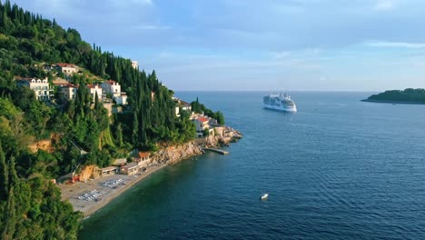 Aerial-shot-of-a-beach-on-the-coast-of-Croatia-with-a-cruise-ship-at-sea,-Europe