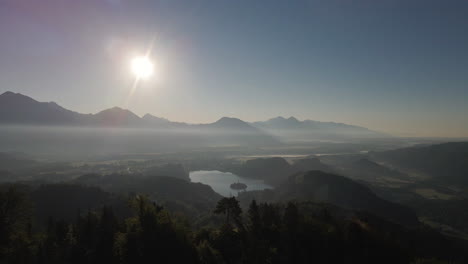 Parallax-shot-showing-Lake-Bled-in-distance-during-sunset,-aerial-view