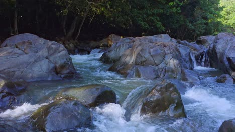 Close-up-shot-of-flowing-water-between-giant-rocks-coming-from-mountains-in-wilderness