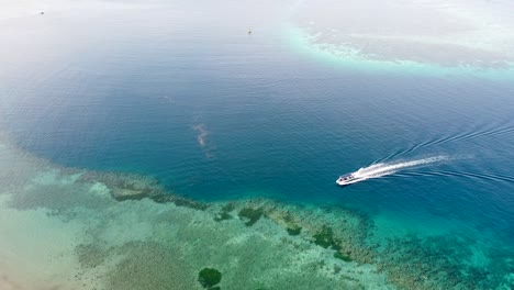 A-dive-boat-moving-through-pristine-ocean-water-and-coral-reefs-leaving-wake-in-its-trail-at-stunning-remote-tropical-island-getaway