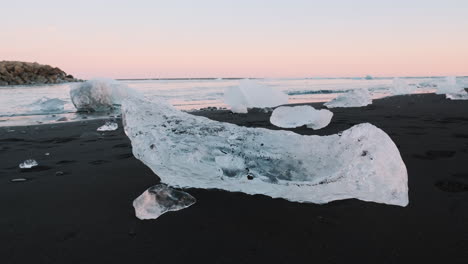 Small-chunks-of-ice-sitting-on-black-sand-of-Diamond-Beach,-Iceland