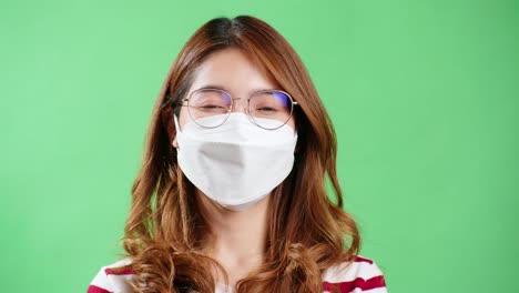 Asian-young-woman-with-eyeglasses-wearing-protective-mask-looking-at-camera-during-studio-recording-with-chroma-key-background