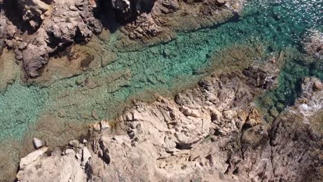 Drone-soars-over-a-rock-in-the-middle-of-the-sandy-beach-of-Chia-in-Sardinia's-south,-stunning-weather